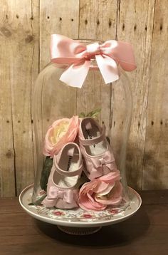 a glass clochet with baby shoes in it and a pink bow on the top