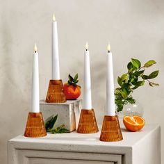 five candles are lined up next to an orange and some other fruit on a table