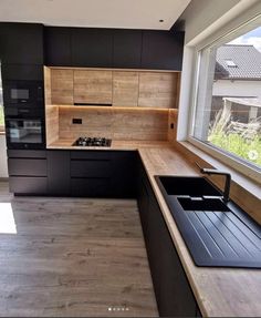 an empty kitchen with black cabinets and wood flooring is seen in this image, looking out the window