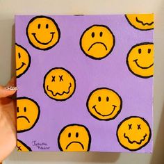 a person holding up a piece of art with yellow smiley faces on purple and white background