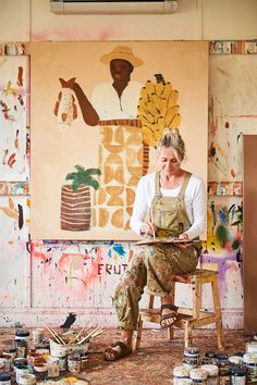 a woman sitting in front of a painting with lots of paint on the walls and floor