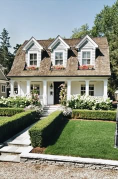 a white house surrounded by hedges and flowers