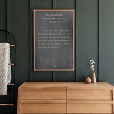 a wooden dresser with a chalkboard on the wall next to it and a plant