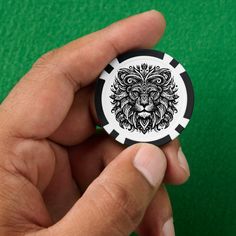 a hand holding a black and white poker chip with a lion head on the front