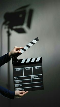 a person holding a clapper in front of a movie camera on a dark background