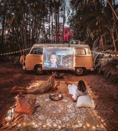 two people sitting on a blanket in front of a vw bus with a screen