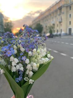 a bouquet of blue and white flowers is held up by someone's hand on the street