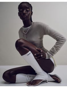 a woman sitting on the ground with her legs crossed and wearing white shoes, in front of a gray background