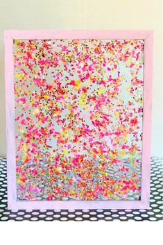 a pink frame filled with confetti sprinkles on top of a black and white checkered tablecloth