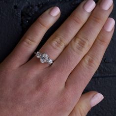 a woman's hand with a three stone ring on her left hand and the other hand holding an engagement ring