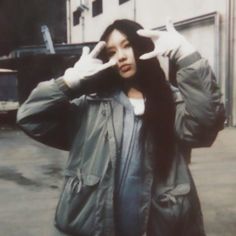 a woman standing in front of a building with her hands up to her face and one hand behind her head