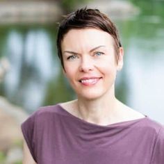 a woman standing in front of a lake wearing a purple shirt and looking at the camera