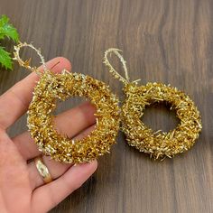 someone is holding two small wreaths made out of tinsel and gold colored wire