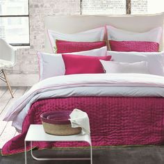 a bed with pink and white comforters in a room next to a brick wall