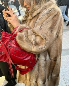 a woman is looking at her cell phone while holding a red purse in her hand