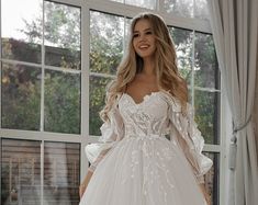 a woman in a white wedding dress standing next to a window