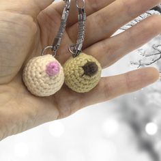 a hand holding two tiny crocheted animals on chain necklaces in front of snow covered branches