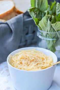 a white bowl filled with cheese next to bread and lettuce on a table