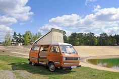 an orange van parked next to a lake with a camper on the back ground