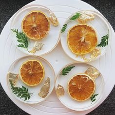 four slices of oranges on plates with leaves and gold leaf decorations are arranged in the shape of circles