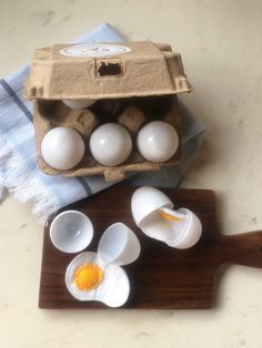 an egg carton filled with white eggs on top of a wooden cutting board next to other eggs