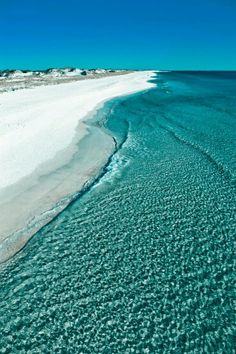 an aerial view of the ocean and beach with white sand, blue water and clear sky