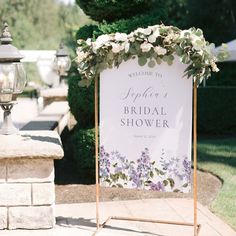 a sign with flowers on it sitting in front of a light pole and lamp post