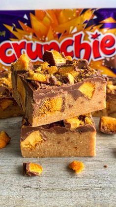 three pieces of chocolate peanut butter crunchie bars stacked on top of each other, with an orange and yellow candy bar in the background