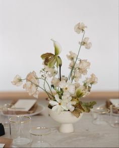 a white vase filled with flowers sitting on top of a table next to wine glasses