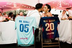 a bride and groom kiss in front of their shirts at the reception table with other guests