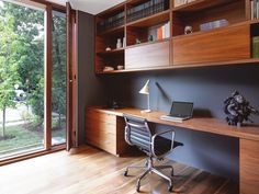 a desk with a laptop on it in front of a large window and wooden shelves