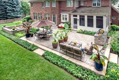 an outdoor patio with tables and chairs in front of a large brick house surrounded by greenery