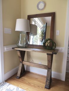 a wooden table with a mirror and lamp on it in front of a door way