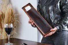 a person holding a brown leather case next to a glass of wine and a knife