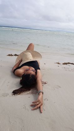 a woman laying on top of a sandy beach next to the ocean wearing a straw hat