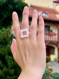 a person's hand with a beaded ring in front of a house and trees