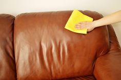 a person cleaning a brown leather couch with a yellow microfibrel cloth on it