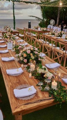 a long wooden table with white plates and flowers on it is set for an outdoor dinner