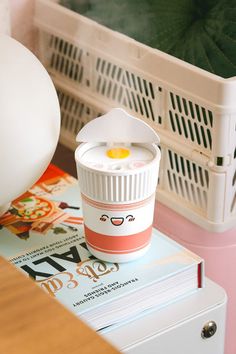 a coffee cup sitting on top of a stack of books next to a white basket