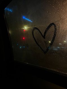 a heart drawn on the side of a window with raindrops and street lights in the background