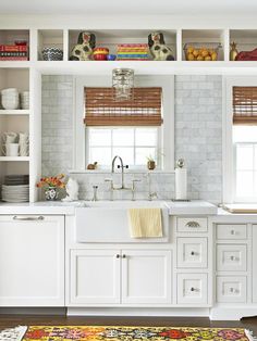 a kitchen with white cabinets and open shelving above the sink is filled with dishes