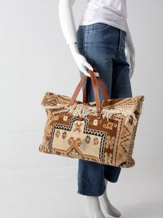 "This classic 1960s handcrafted bag was made with a gorgeous wool carpet. The boho overnight bag features warm brown, gold, and cream tones, a fringed flip-over closure and double leather handles. An iconic fashion statement.  CONDITION In good condition with wear consistent with age and use.  Faint dark spot on front.  General wear to the leather and fabric.  MEASUREMENTS Length: 22\"  ..  55.9 cm Width:  5\"  ..  12.7 cm Height: 13.5\"  ..  34.3 cm Drop:  4.5\"  ..  11.4 cm 223156" Brown Bohemian Tote Travel Bag, Bohemian Brown Tote Travel Bag, Bohemian Brown Weekender Bag With Leather Handles, Vintage Rectangular Fringe Bag, Bohemian Brown Rectangular Travel Bag, Vintage Brown Tote Weekender Bag, Handmade Travel Bag, Victorian Carpet, Pucci Vintage