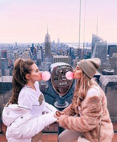 two young women sitting on top of a building with bubble gums in their mouths