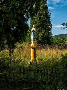 a statue in the middle of a field with tall grass and trees behind it on a sunny day