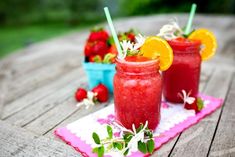 two drinks are sitting on a table with strawberries and oranges