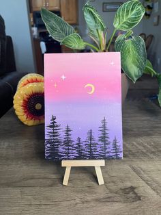 an easel with a painting on it and a potted plant in the background