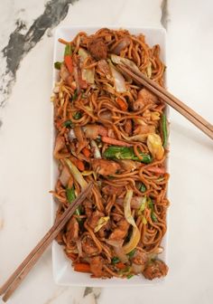 stir fry noodles with meat and vegetables on a white plate next to chopsticks