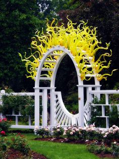 a white sculpture with yellow flowers on it in the middle of a flower garden area