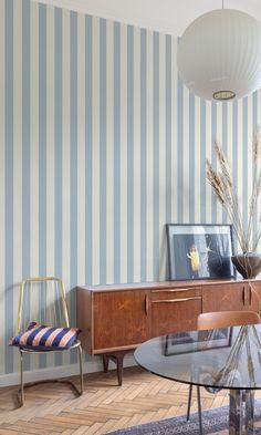 a living room with striped walls and wooden furniture in the corner, along with a glass top dining table