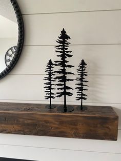 a mirror and some black trees on a shelf in front of a white painted wall